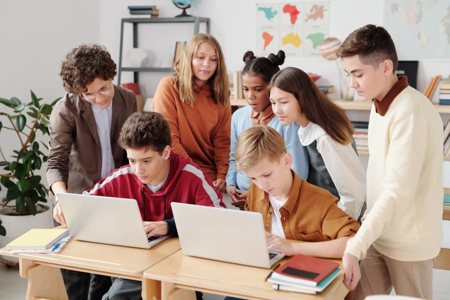 High school students collaborating on classroom laptops with a teacher