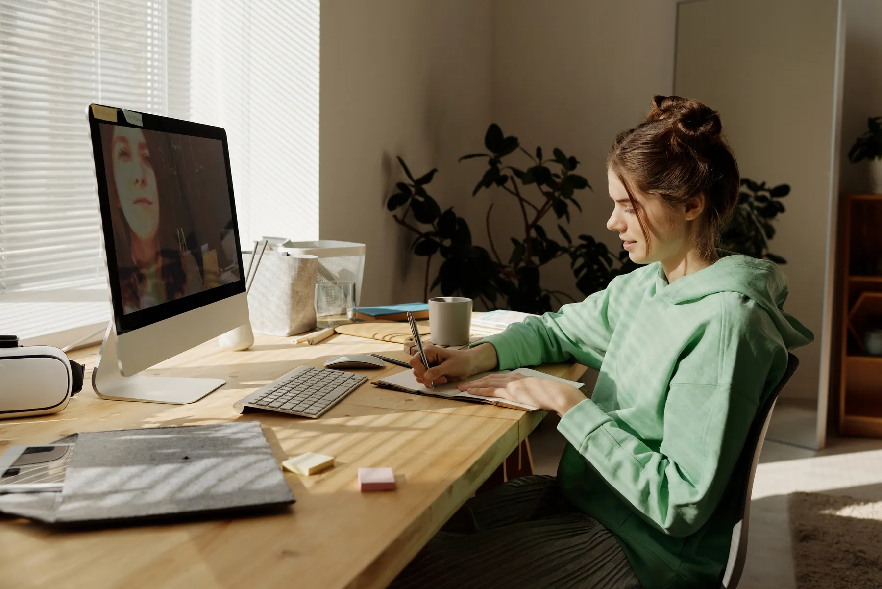 College student taking notes during a live online class at a study desk